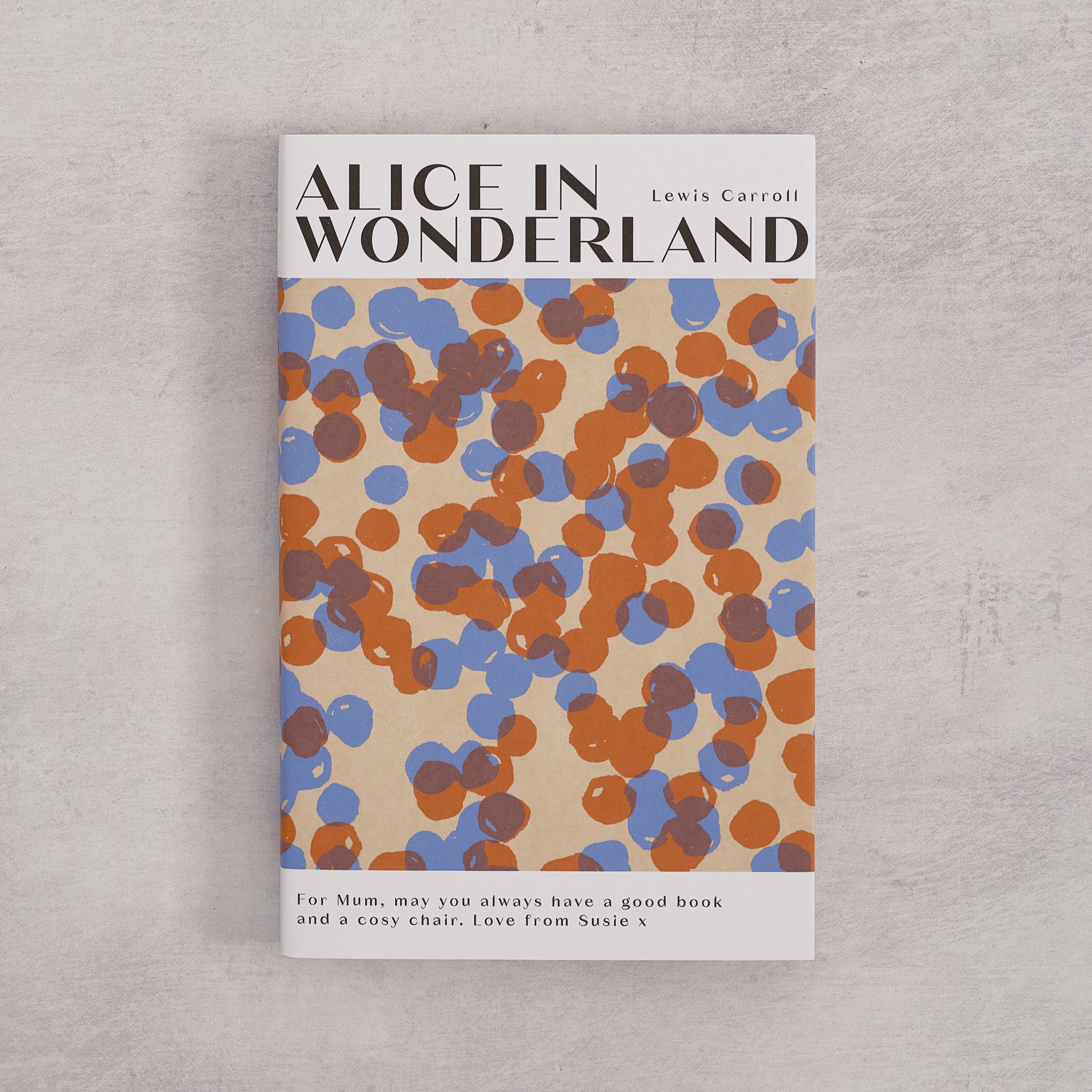 Bookishly edition of Alice in Wonderland by Lewis Carroll with a blue and rust dot-patterned dust jacket and personalised message printed on the front cover.