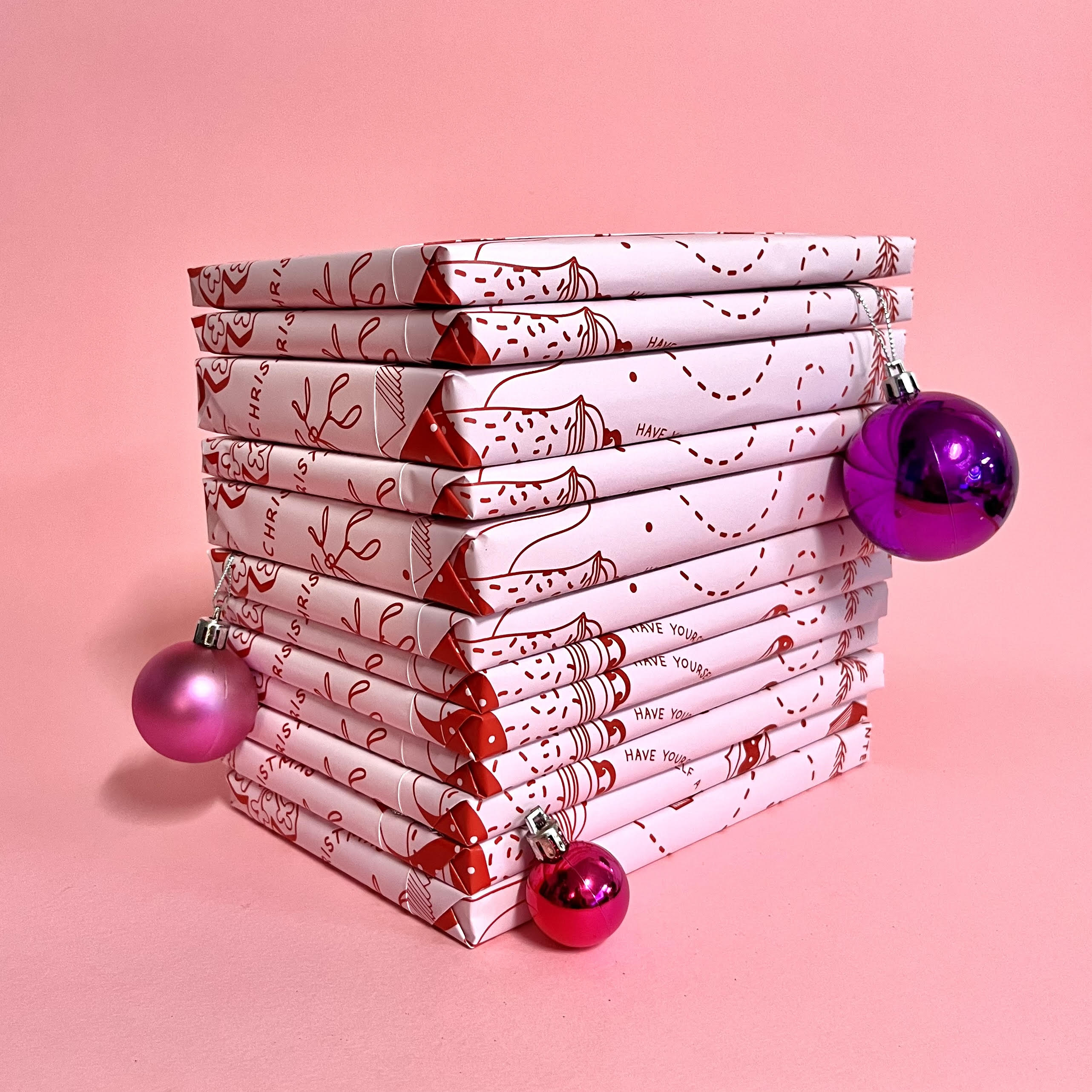 Stack of twelve individually wrapped books from the Bookishly book advent calendar, decorated with pink and red festive paper and Christmas baubles.