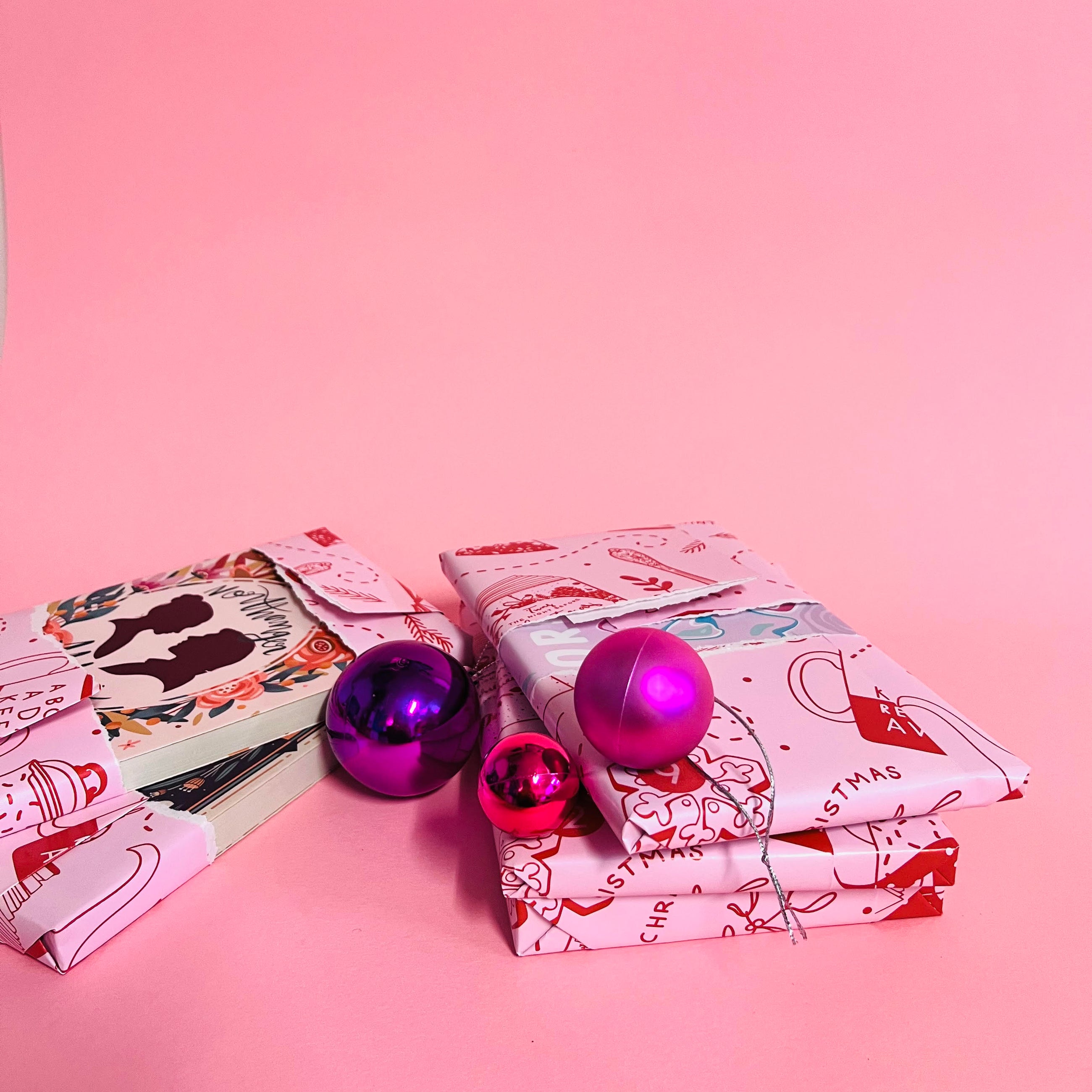 Partly unwrapped books from the Bookishly book advent calendar, showing custom dust jackets with pink and purple baubles on a pink background.