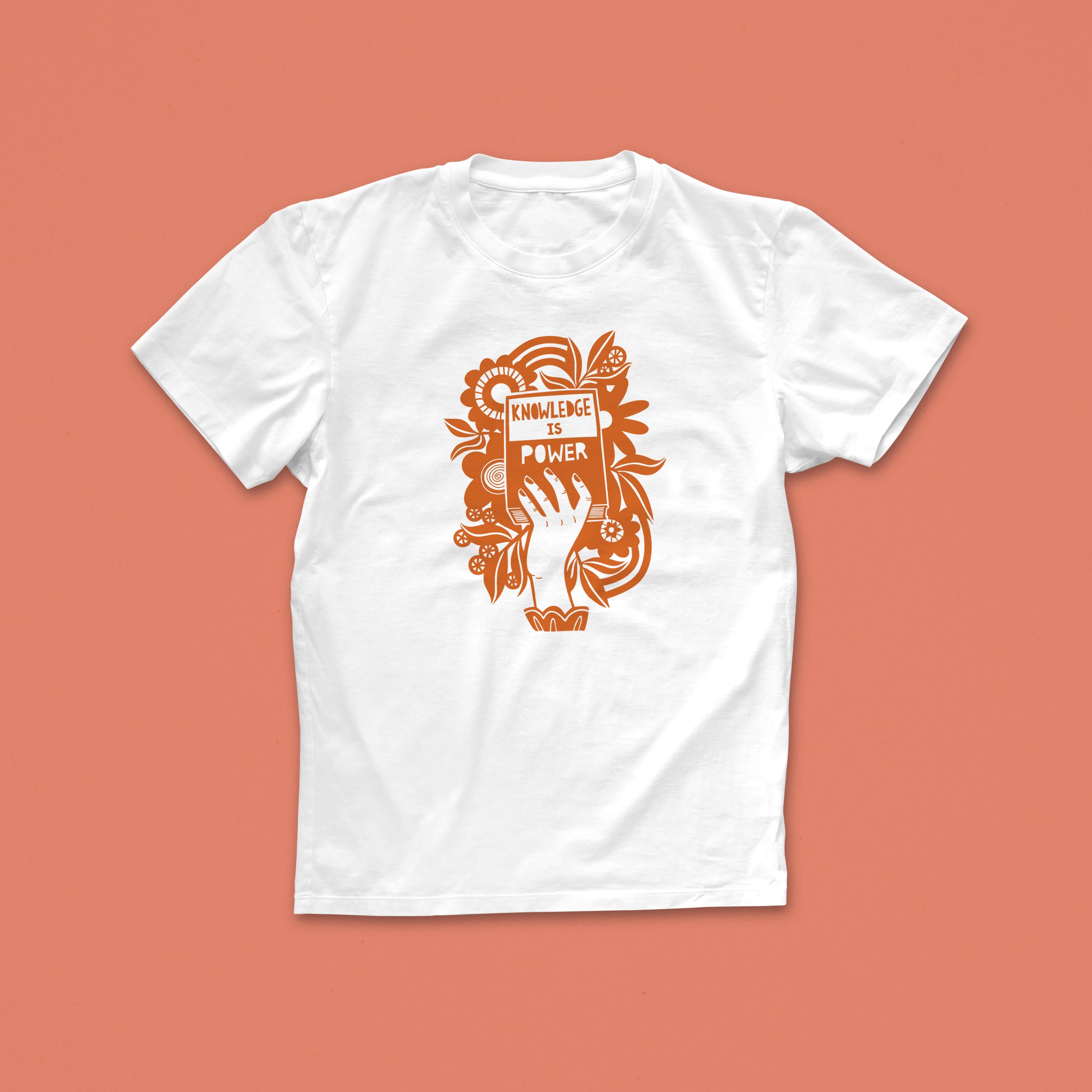 Knowledge Is Power T-shirt with hand-drawn illustration of a raised hand holding a book in rust-orange, surrounded by flowers and bold text