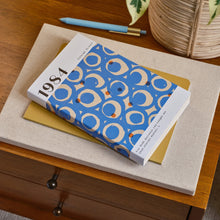 Book with a blue and white cover on a wooden surface with a plant in the background