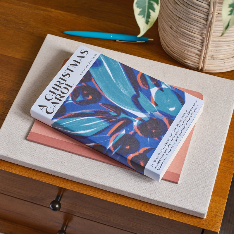 Book titled 'A Christmas Carol' on a wooden surface with a plant in the background
