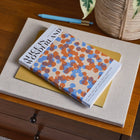 Book titled 'Alice In Wonderland' with colorful cover on a wooden surface with a plant in the background