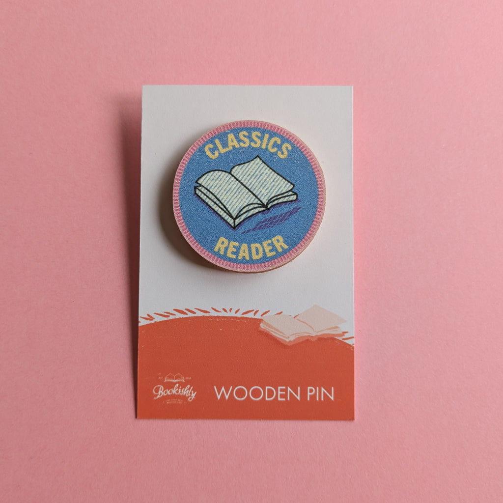 Classics Reader wooden pin on a pink background, featuring an open book on a round blue badge with pink edging.
