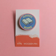 Classics Reader wooden pin on a pink background, featuring an open book on a round blue badge with pink edging.