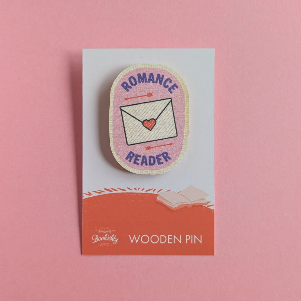 Romance Reader wooden pin on a pink background, featuring a love letter and arrows on a pink badge design.