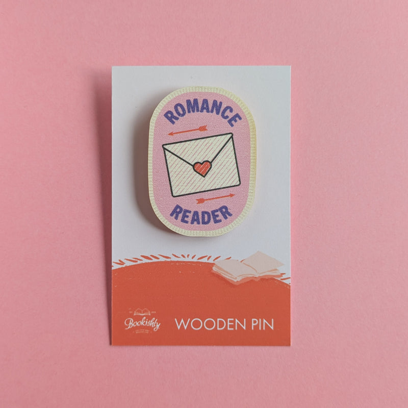 Romance Reader wooden pin on a pink background, featuring a love letter and arrows on a pink badge design.