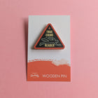 True Crime Reader wooden pin on a pink background, shaped like a red warning triangle with a chalk outline graphic.