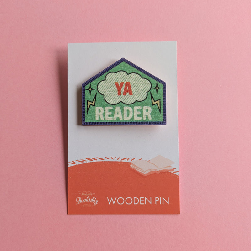 YA Reader wooden pin on a pink background, featuring a green stitched badge with a comic-style cloud and lightning bolts.