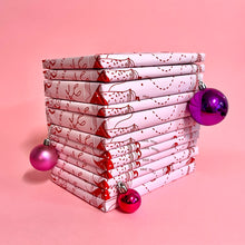 Stack of twelve individually wrapped books from the Bookishly book advent calendar, decorated with pink and red festive paper and Christmas baubles.