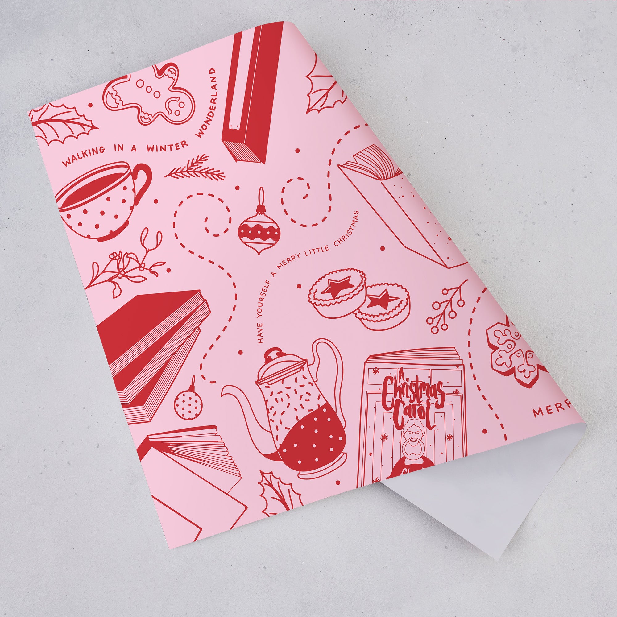 Pink and red Christmas wrapping paper sheet with bookish festive doodle illustrations including books, mugs, decorations, and biscuits.