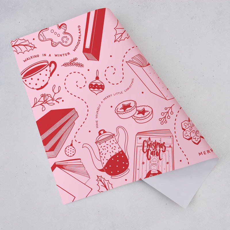 Pink and red Christmas wrapping paper sheet with bookish festive doodle illustrations including books, mugs, decorations, and biscuits.