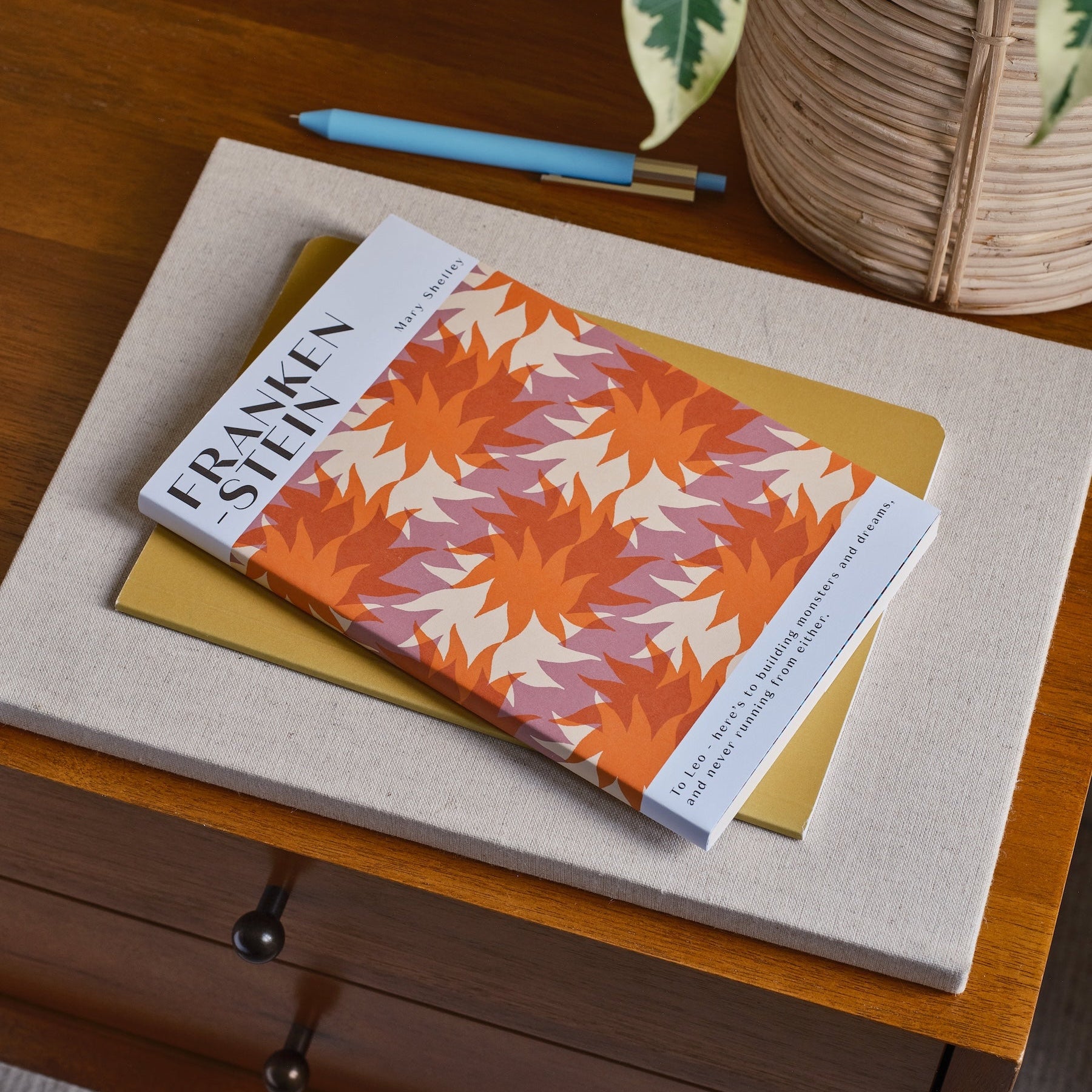 Book titled 'Frankenstein' with a colorful cover on a wooden surface next to a plant.