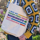 Person holding a tote bag with colorful text in an outdoor setting