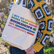 Person holding a tote bag with colorful text in an outdoor setting