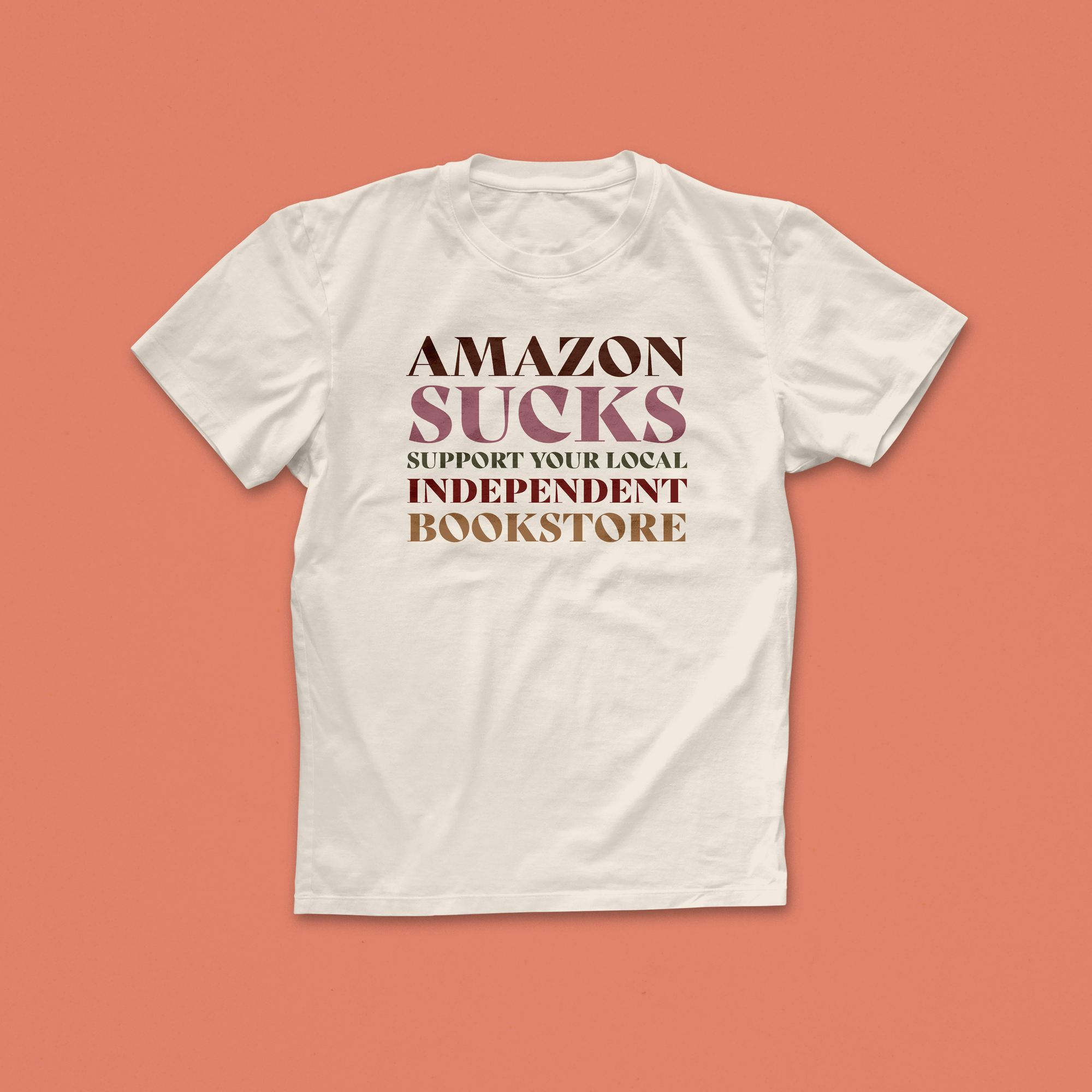 Amazon Sucks T-shirt with bold retro text in pink and brown, encouraging support for local independent bookstores