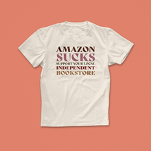 Amazon Sucks T-shirt with bold retro text in pink and brown, encouraging support for local independent bookstores