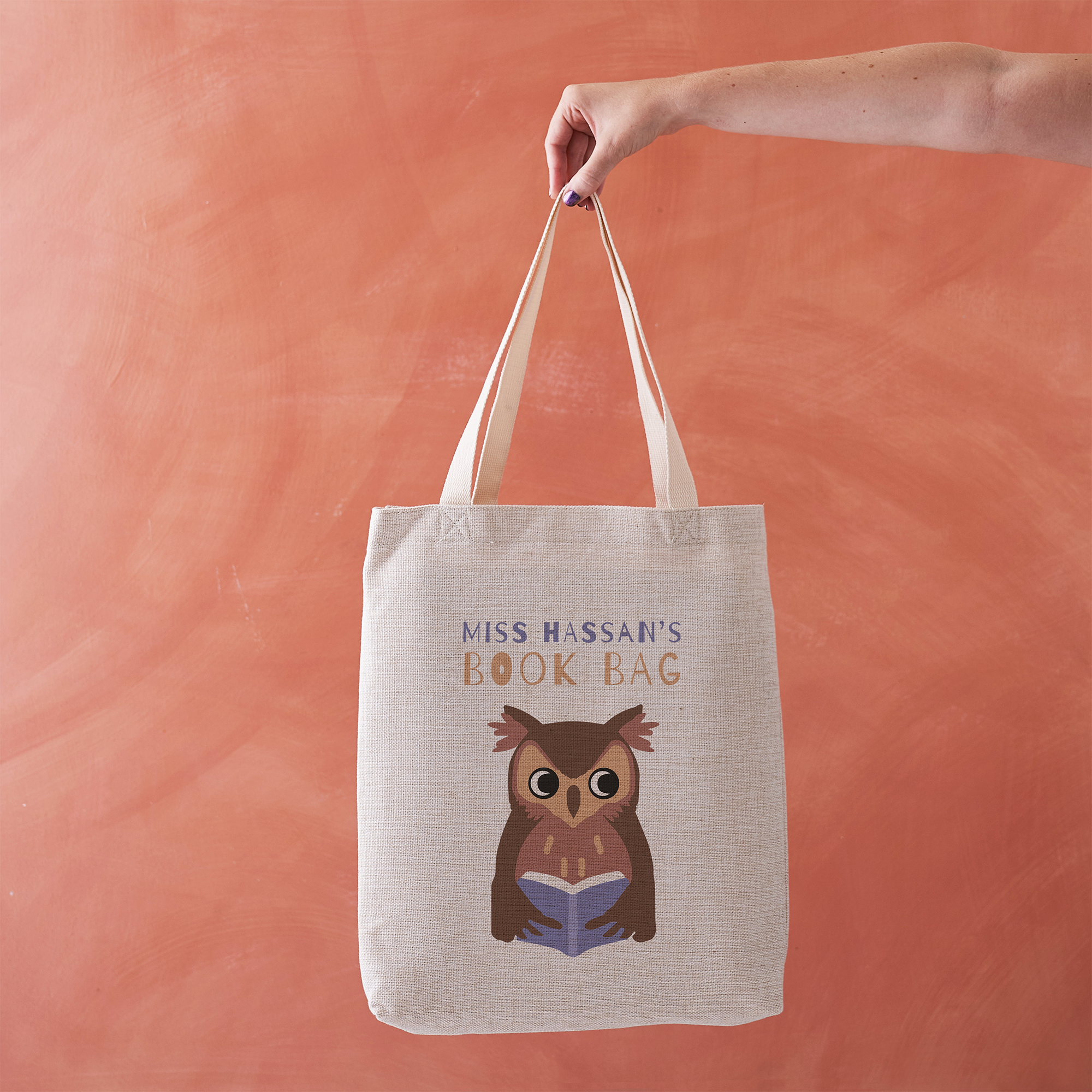 Tote bag with owl design and text held against a peach background