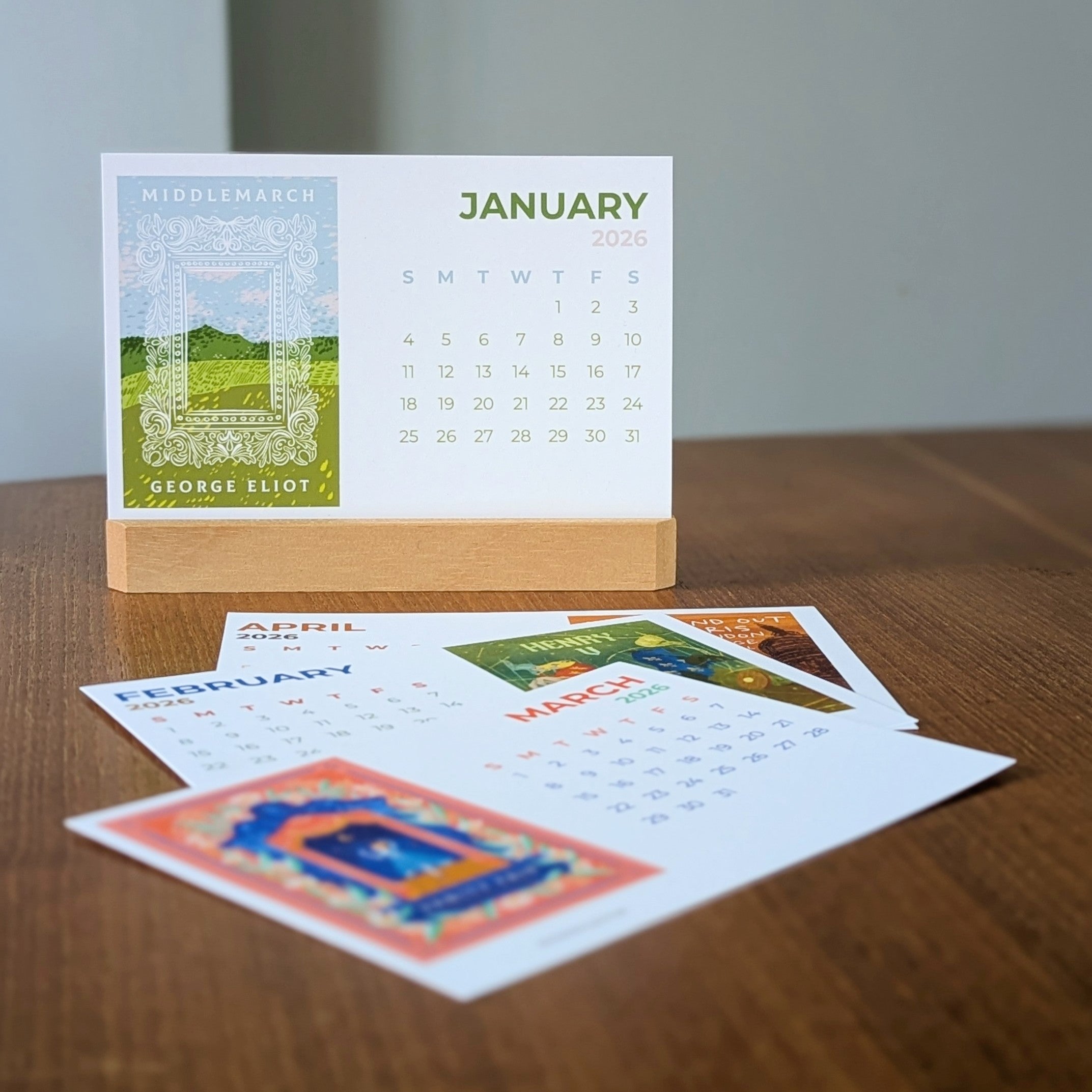 2026 Book Cover Calendar Postcard Set displayed on wooden holder, showing January design and colourful literary postcards on a desk.