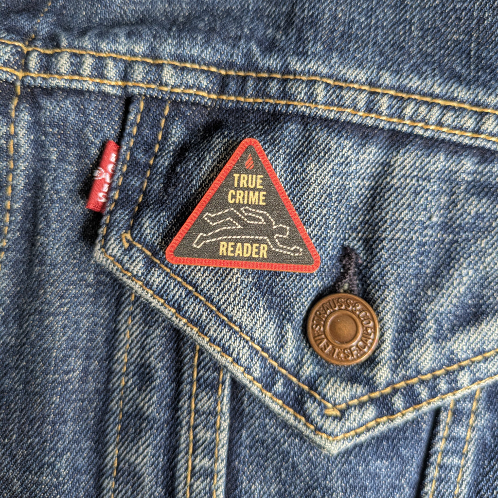 True Crime Reader wooden pin attached to the pocket of a denim jacket.