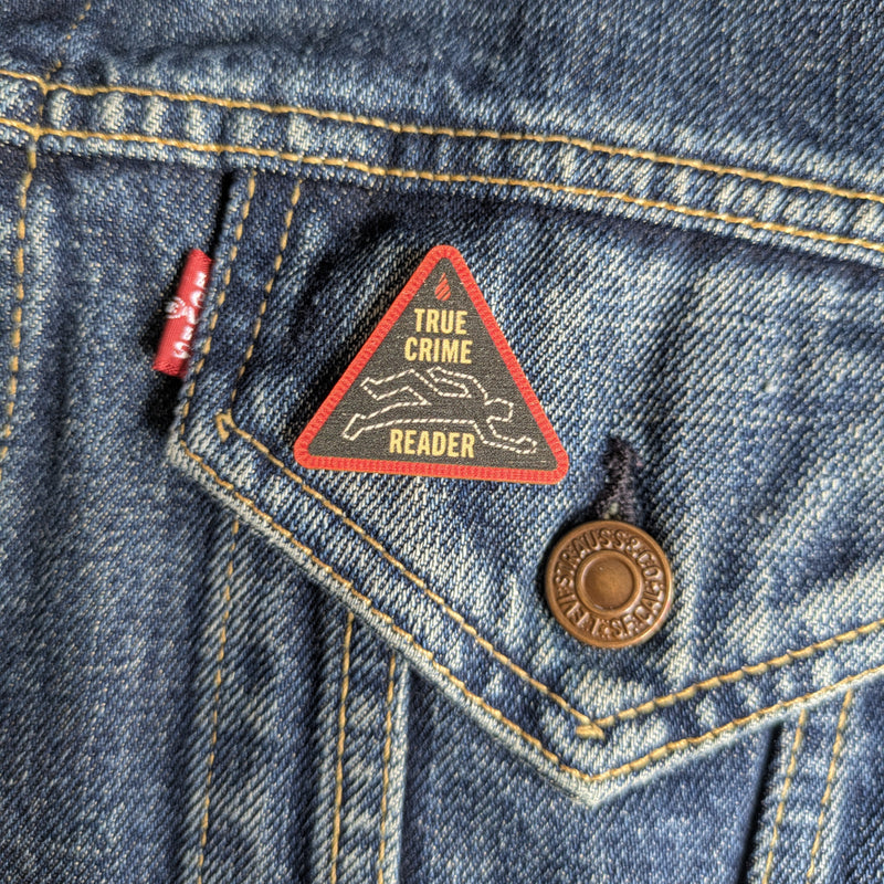 True Crime Reader wooden pin attached to the pocket of a denim jacket.