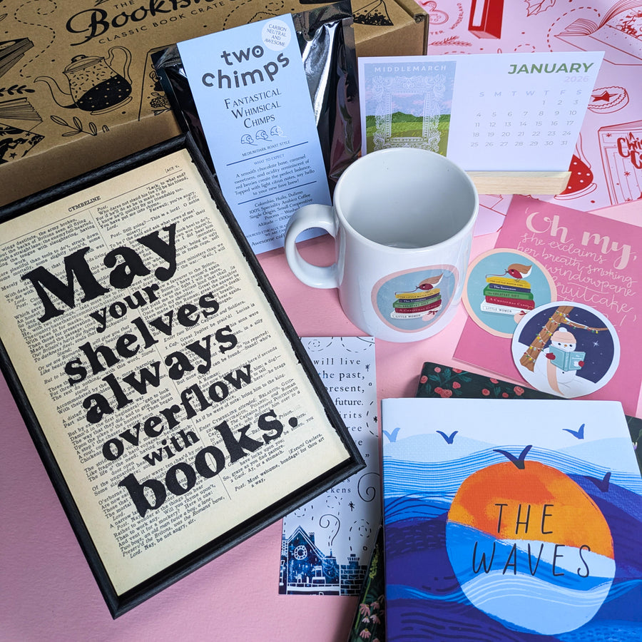A winter-themed gift box for readers displayed on a pink background, with a framed book page print, classic novel, festive mug, speciality coffee, 2026 postcard calendar, bookmarks, postcards and seasonal stickers.