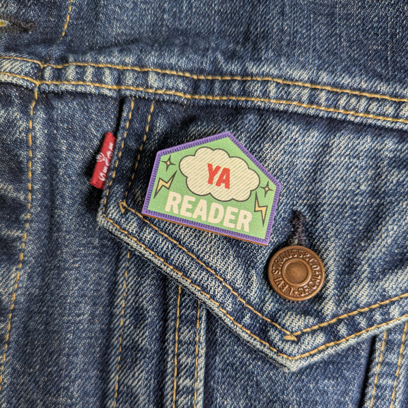YA Reader wooden pin attached to the pocket of a denim jacket.