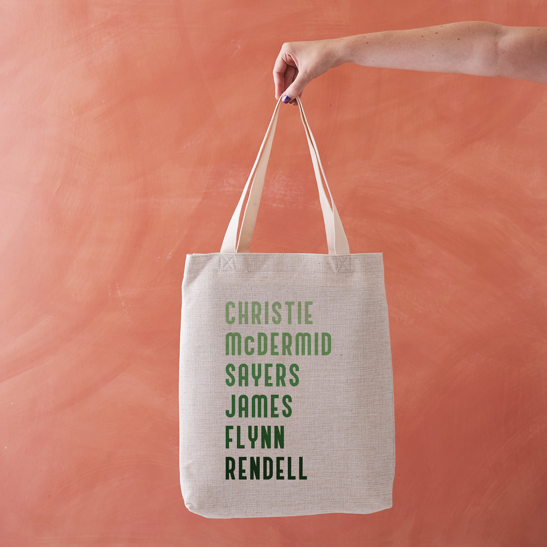 Natural linen-effect tote bag with green text listing female crime authors, held against a coral background