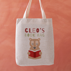 Tote bag with bear holding a book design and 'Cleo's Book Bag' text on an orange background
