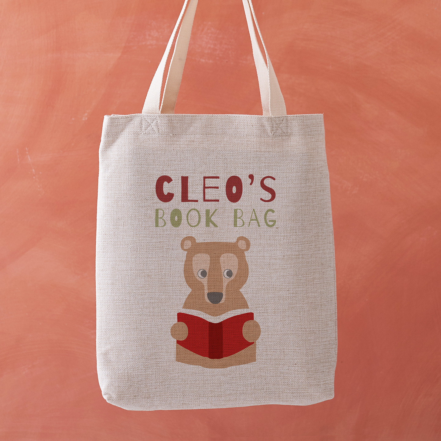 Tote bag with bear holding a book design and 'Cleo's Book Bag' text on an orange background