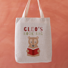 Tote bag with bear holding a book design and 'Cleo's Book Bag' text on an orange background