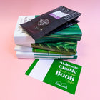 Stack of classic crime and thriller books with Bookishly-designed covers, a sachet of Perkulatte coffee, and a green welcome card from the Classic Crime & Thriller Book Club, on a pink background.