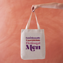 Linen effect tote bag with the phrase “Emotionally Unavailable Fictional Men” in red and purple lettering, held against a warm terracotta background.