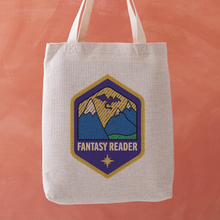 Fantasy Reader tote bag with a stitched badge-style design featuring a mountain range illustration on a deep purple background.
