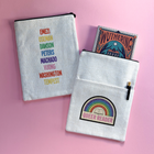 Double-sided Queer Reader book sleeve with rainbow badge design on one side and LGBTQ+ author list in rainbow text on the other, styled on a pink background.