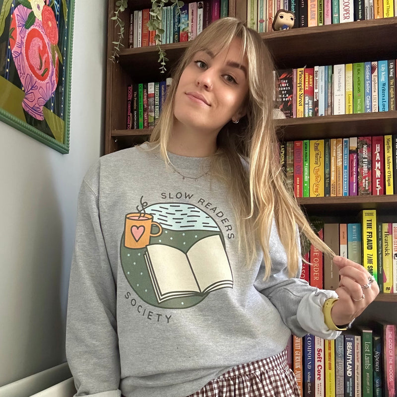 Person wearing a 'Slow Readers Society' sweatshirt in front of a bookshelf.