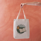 Natural-coloured tote bag with “Slow Readers Society” design featuring an open book, night sky, and illustrated mug.