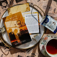 Book titled 'The Wall of Loneliness' by Radclyffe Hall on a plate with tea and cookies.