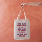 Linen-effect tote bag with a list of romance tropes printed in red, pink, and purple text, held against a warm terracotta background.