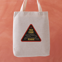 True Crime Reader tote bag with a stitched badge-style design featuring a chalk outline illustration in yellow on a black background.
