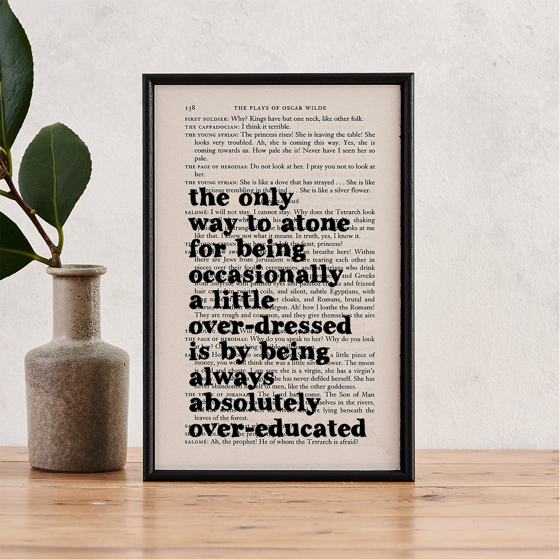 Framed book page print with Oscar Wilde quote: “The only way to atone for being occasionally a little overdressed is by being always absolutely overeducated,” printed on a play script page.