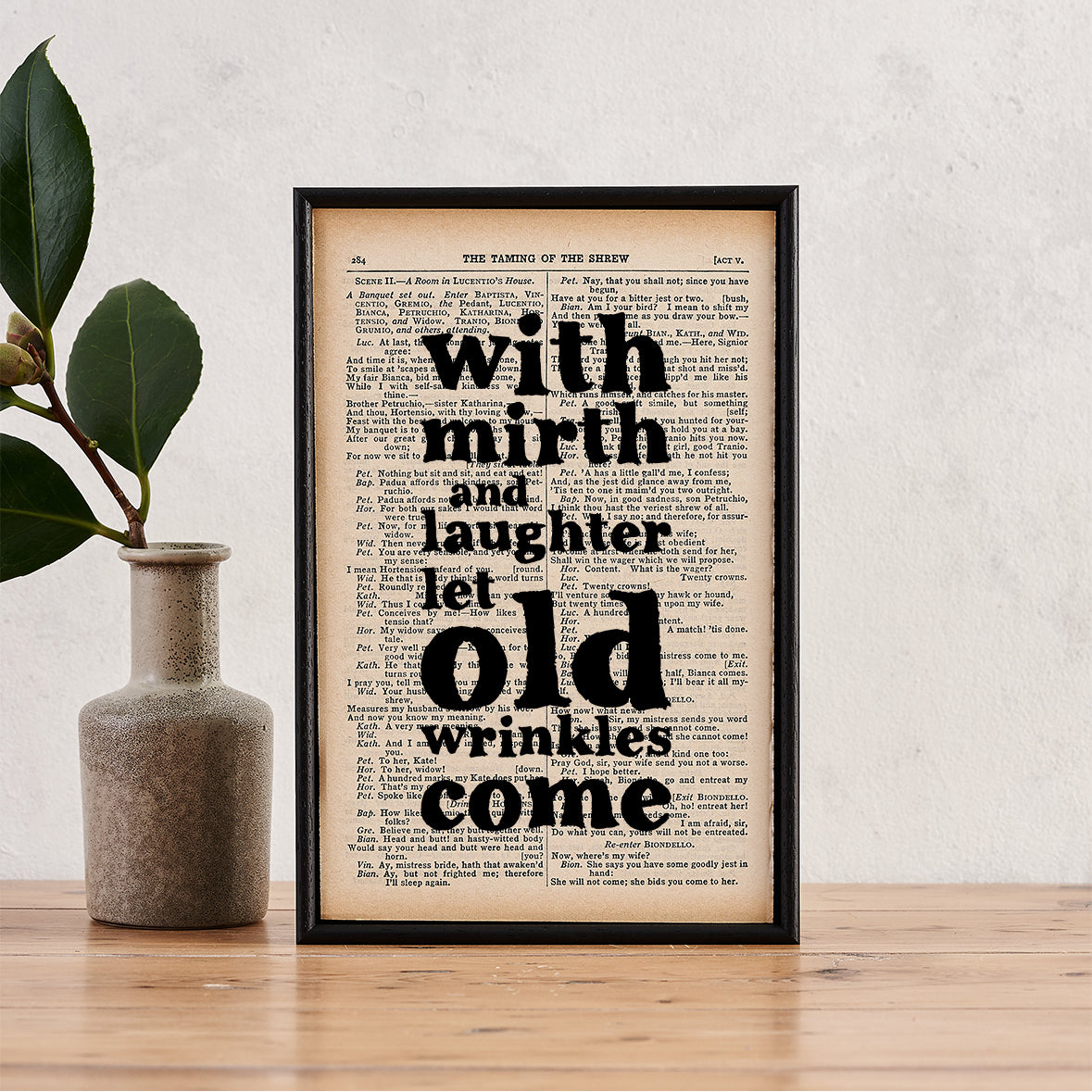 Framed book page print with the quote “With mirth and laughter let old wrinkles come” printed in bold black type onto a page from The Complete Works of William Shakespeare.